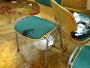 Drei polsterbezogene Holzstühle stehen auf einem Parkettboden in einem Raum, der mit Blutflecken bespritzt ist.