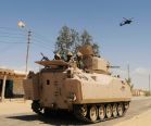 Egyptian Army soldiers patrol in an armored vehicle backed by a helicopter gunship in Sheikh Zuweid
